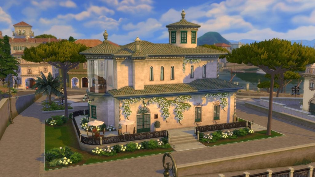 A sunlit Mediterranean-style home with ivy-covered walls, green shutters, and a tiled roof sits along a quiet waterfront street.