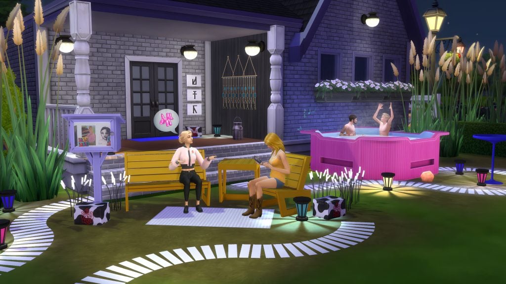 Nighttime backyard scene with Sims chatting on benches, decorative lights and plants, and two Sims relaxing in a pink outdoor hot tub.